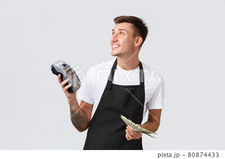 Small retail business, payments and employees concept. Friendly handsome waiter, serving tables, barista giving customer POS terminal and money, looking left, white background Small retail business, payments and employees concept. Friendly handsome waiter, serving tables, barista giving customer POS terminal and money, looking left, white background 80874433