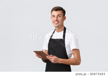 Small business, coffee shop and cafe employees concept. Handsome waiter, barista wearing apron, taking order, saving tables with digital tablet, smiling at camera, white background 80875683