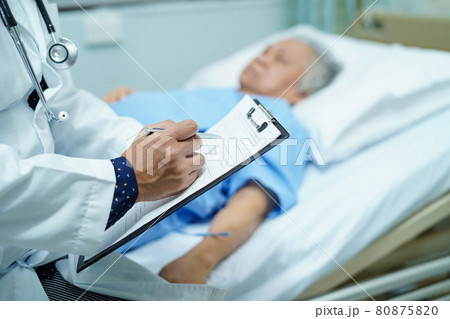 Doctor writing down the diagnosis on clipboard while Asian senior or elderly old lady woman  lying on bed in nursing hospital ward : healthy strong medical concept.. 80875820
