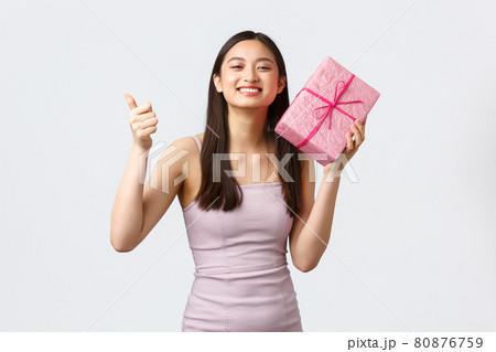 Celebration, party and holidays concept. Pleased happy beautiful birthday girl in evening dress, show thumbs-up and thanking for awesome gift, holding present box, white background Celebration, party and holidays concept. Pleased happy beautiful birthday girl in evening dress, show thumbs-up and thanking for awesome gift, holding present box, white background 80876759