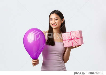 Celebration, party and holidays concept. Beautiful asian girl in evening dress, smiling pleased, enjoying celebrating birthday, holding b-day gift and balloon, congratulating, white background 80876835