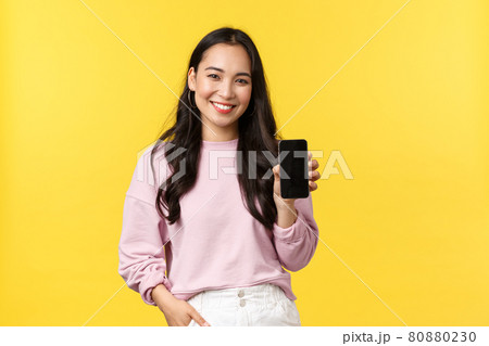 People emotions, lifestyle leisure and beauty concept. Smiling asian woman 20s, showing smartphone display, recommend application or mobile game, advertisement on screen, yellow background People emotions, lifestyle leisure and beauty concept. Smiling asian woman 20s, showing smartphone display, recommend application or mobile game, advertisement on screen, yellow background 80880230