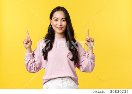 People emotions, lifestyle and fashion concept. Pleasant smiling attractive woman in stylish clothes pointing fingers up, demonstrate product link, advertising over yellow background People emotions, lifestyle and fashion concept. Pleasant smiling attractive woman in stylish clothes pointing fingers up, demonstrate product link, advertising over yellow background 80880232