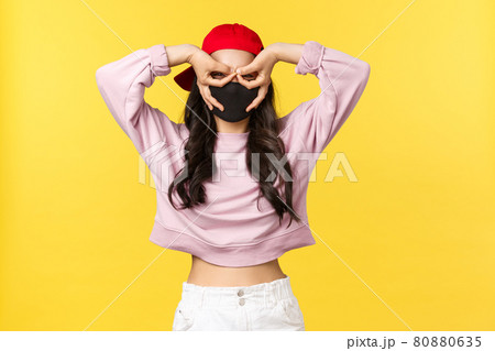 Covid-19, social-distancing lifestyle, prevent virus spread concept. Funny and cute asian girl in face mask and red cap, make fake glasses with fingers over eyes, stare surprised and impressed Covid-19, social-distancing lifestyle, prevent virus spread concept. Funny and cute asian girl in face mask and red cap, make fake glasses with fingers over eyes, stare surprised and impressed 80880635