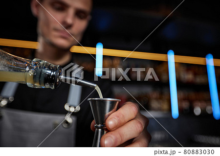 Bartender in apron adds ingredient to shaker 80883030