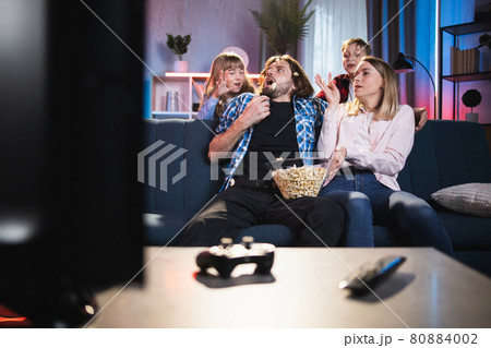 Playful children scaring parents that were watching TV Playful children scaring parents that were watching TV 80884002