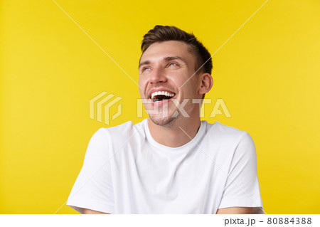 Lifestyle, summer and people emotions concept. Close-up portrait of carefree happy handsome man, looking upper left corner banner and laughing, standing in basic white t-shrit over yellow background 80884388
