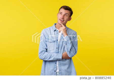 Thoughtful intrigued handsome blond man making choice in store, looking curious at upper left corner, touching chin and squinting while picking product on shelf, standing yellow background Thoughtful intrigued handsome blond man making choice in store, looking curious at upper left corner, touching chin and squinting while picking product on shelf, standing yellow background 80885240