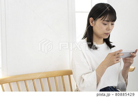 部屋で椅子に座ってスマホを操作する女性 80885429