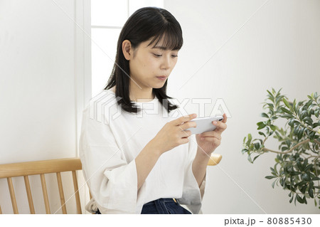 部屋で椅子に座ってスマホを操作する女性 80885430