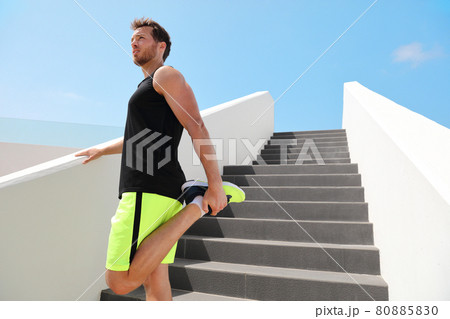 Leg muscles stretch fit man runner getting ready to run stretching legs warm-up quad stretches exercises on outdoor stairs for cardio HIIT summer workout. Leg muscles stretch fit man runner getting ready to run stretching legs warm-up quad stretches exercises on outdoor stairs for cardio HIIT summer workout. 80885830