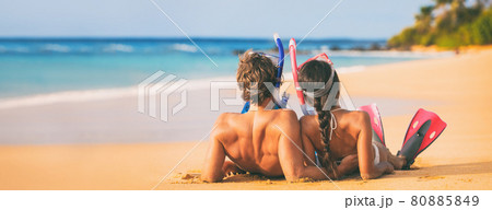 Beach couple relaxing on summer honeymoon vacation with snorkel equipment. People lying down on golden sand at sunset with diving mask, flippers sun tanning enjoying travel holiday lifestyle. Beach couple relaxing on summer honeymoon vacation with snorkel equipment. People lying down on golden sand at sunset with diving mask, flippers sun tanning enjoying travel holiday lifestyle. 80885849