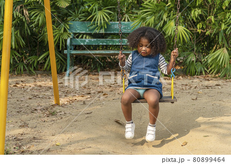 Adorable dark skinned toddler daughter mixed-race playing swing in playground looking something 80899464