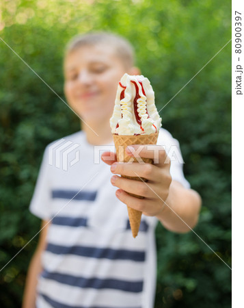 Teenager boy eating ice-cream cone on green nature background. Summer, junk food and people concept. Focus on hand 80900397
