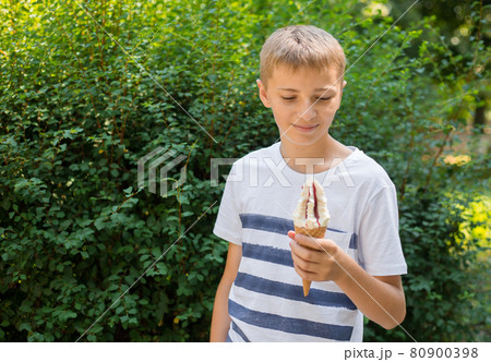 Teenager boy eating ice-cream cone on green nature background. Summer, junk food and people concept. Copyspace Teenager boy eating ice-cream cone on green nature background. Summer, junk food and people concept. Copyspace 80900398