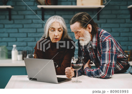 Happy senior couple using laptop at the kitchen Happy senior couple using laptop at the kitchen 80903993