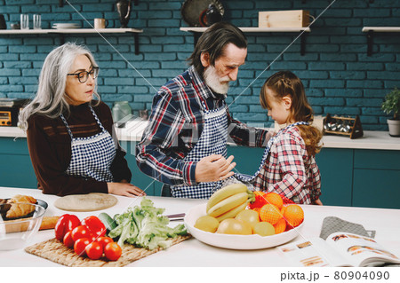 Senior grandparents couple with dgranddaughter cooking in kitchen Senior grandparents couple with dgranddaughter cooking in kitchen 80904090
