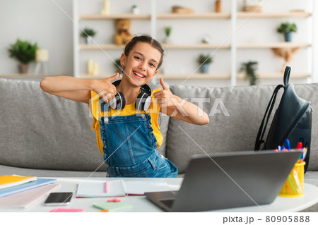 Girl sitting at desk, using pc, showing thumbs up Girl sitting at desk, using pc, showing thumbs up 80905888