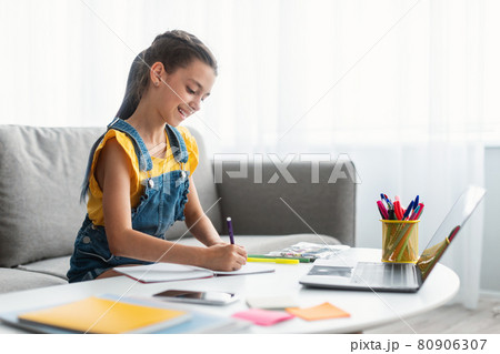 Girl sitting at desk, drawing in copybook Girl sitting at desk, drawing in copybook 80906307