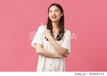 Beauty, people emotions and summer leisure concept. Charismatic attractive glamour asian woman in dress pointing upper left corner, smiling and laughing from joy, pink background 80906743