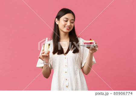 Celebration, party holidays and fun concept. Dreamy beautiful woman celebrating her birthday with glass champagne and b-day cake, smiling carefree at dessert, standing pink background Celebration, party holidays and fun concept. Dreamy beautiful woman celebrating her birthday with glass champagne and b-day cake, smiling carefree at dessert, standing pink background 80906774