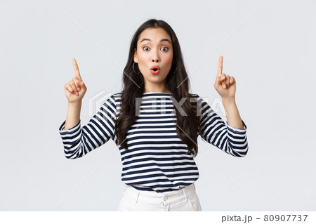 Lifestyle, beauty and fashion, people emotions concept. Surprised and intrigued attractive korean girl shopping, found good sale, pointing fingers up at top banner and say wow 80907737