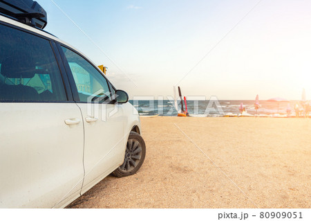 Side view of big family white suv van car with big rooftop cargo rack box at scenic sand seaside campsite camp coast of sea or ocean sky on background. Accessory rental travel trip vacation concept 80909051