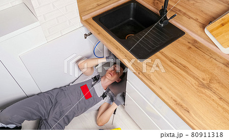 Employee unscrews details repairing waste trap under sink Employee unscrews details repairing waste trap under sink 80911318