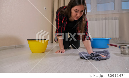 Disappointed lady wipes water with rug from floor in room Disappointed lady wipes water with rug from floor in room 80911474