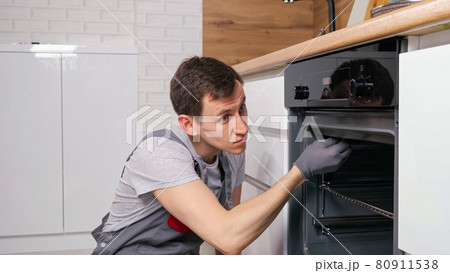 Skilled employee twists screw on broken oven repairing Skilled employee twists screw on broken oven repairing 80911538