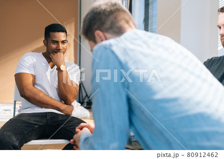 Close-up back view of depressed young man sharing mental problem sitting in circle to other patients during group therapy session. 80912462