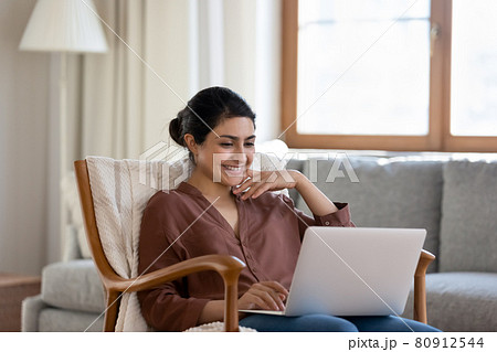Smiling ethnic woman use laptop relaxing at home Smiling ethnic woman use laptop relaxing at home 80912544
