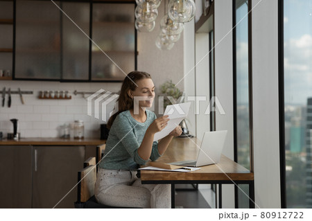 Happy young woman reading paper letter at home workplace Happy young woman reading paper letter at home workplace 80912722