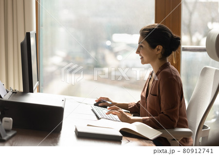 Smiling Indian woman work on computer in office Smiling Indian woman work on computer in office 80912741