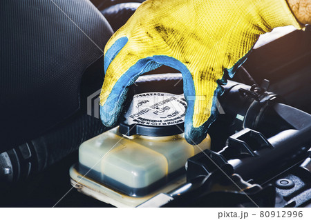 The mechanic hand is open or close the cap of the power steering fluid to check the hydraulic fluid level 80912996