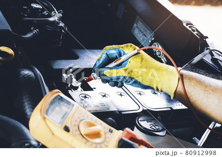 Technician to checking voltage stable of the car battery with digital multimeter probe 80912998