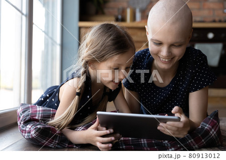 Happy little daughter kid and hairless cancer mom using tablet Happy little daughter kid and hairless cancer mom using tablet 80913012