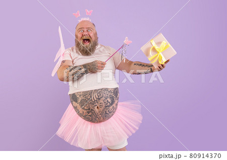 Excited obese male person in fairy costume holds gift box on purple background 80914370