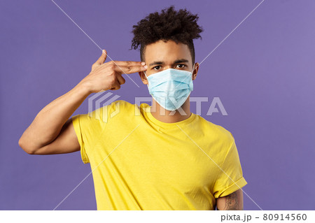 Covid19, healtcare and medicine concept. Close-up portrait of serious hispanic guy in medical mask, showing gun near head as if sick and tired of people not avoid social contact, purple background Covid19, healtcare and medicine concept. Close-up portrait of serious hispanic guy in medical mask, showing gun near head as if sick and tired of people not avoid social contact, purple background 80914560