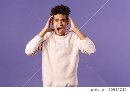 Portrait of scared and anxious young hispanic handsome man in panic, shaking hands nead head, screaming and gasping afraid, being in trouble, standing alarmed over purple background 80915213