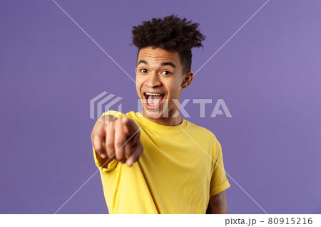 Close-up portrait of upbeat, amazed hispanic man with dreads, young student pointing finger at camera and laughing, recognize someone familiar, standing purple background Close-up portrait of upbeat, amazed hispanic man with dreads, young student pointing finger at camera and laughing, recognize someone familiar, standing purple background 80915216