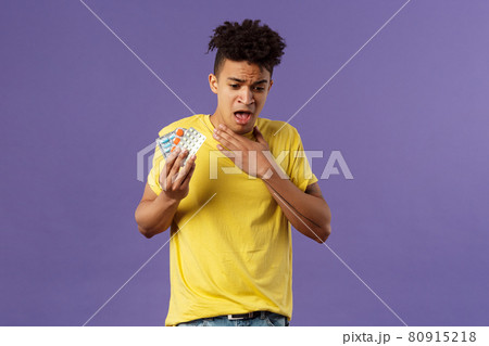 Health, influenza, covid-19 concept. Portrait of young man coughing, choking with tablet, drank pill without water, holding drugs and touch neck as suffer sore throat, purple background 80915218