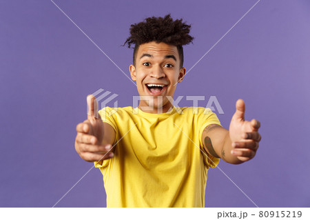 Close-up portrait of charismatic, happy friendly-looking hispanic man with dreads reaching hands forward to hold something, give hug or cuddle dearly, standing purple background 80915219