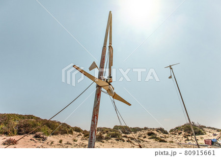 Two small wind turbines, one of them broken, standing on desert, strong back light sun in background. 80915661