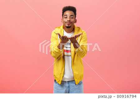 Blowing you sweet kisses. Cute and handsome stylish man with beard and afro hairstyle bending towards camera folding lips and smiling sending mwah with hands near breast over pink background Blowing you sweet kisses. Cute and handsome stylish man with beard and afro hairstyle bending towards camera folding lips and smiling sending mwah with hands near breast over pink background 80916794