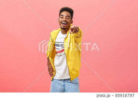 ha-ha loser. Portrait of happy amused energetic african american bearded male in yellow trendy jacket pointing at camera with index finger and laughing out loud humiliating mocking strange weirdo ha-ha loser. Portrait of happy amused energetic african american bearded male in yellow trendy jacket pointing at camera with index finger and laughing out loud humiliating mocking strange weirdo 80916797
