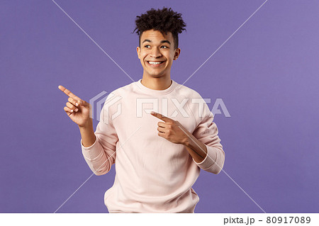 Portrait of enthusiastic, good-looking hispanic man with dreads, looking and pointing upper left corner with satisfied beaming smile, seeing cool thing, made his choice, purple background 80917089