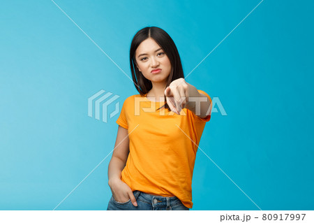 Disappointed attractive asian girl frowning, grimasing upset, pointing index finger camera upset unsatisfied, disliking you, accuse someone, blame person, standing displeased blue background 80917997