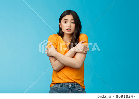 Girl feeling uncomfortable walking light yellow t-shirt, hugging herself trembling, shaking feeling cold, freezing windy weather, frowning grimacing discomfort, stand blue background Girl feeling uncomfortable walking light yellow t-shirt, hugging herself trembling, shaking feeling cold, freezing windy weather, frowning grimacing discomfort, stand blue background 80918247