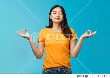 Peaceful charming relaxed asian girl buddhist meditating, breathing, inhale fresh air practice yoga, close eyes smiling relieved, stand lotus nirvana pose, reach zen, standing blue background Peaceful charming relaxed asian girl buddhist meditating, breathing, inhale fresh air practice yoga, close eyes smiling relieved, stand lotus nirvana pose, reach zen, standing blue background 80918317